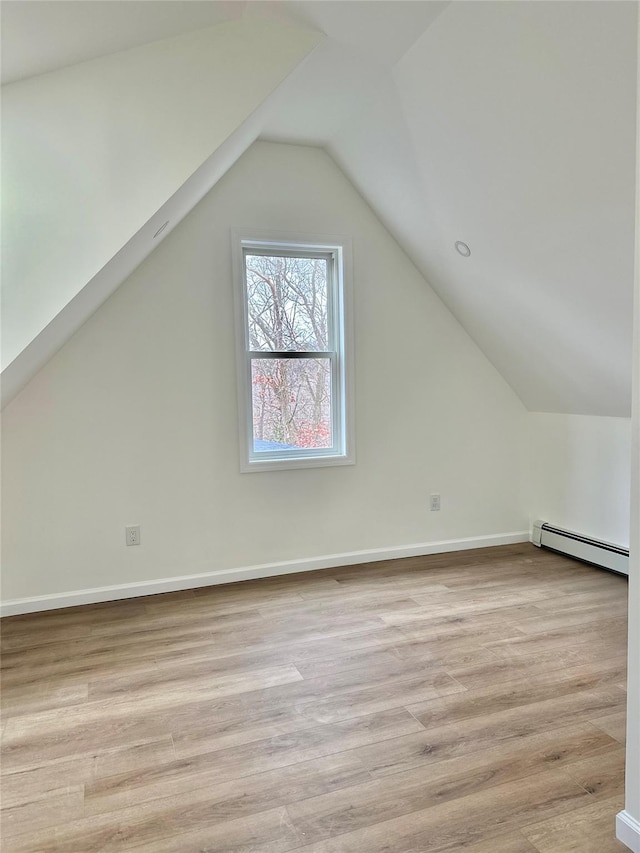 additional living space featuring baseboards, vaulted ceiling, light wood-style flooring, and baseboard heating