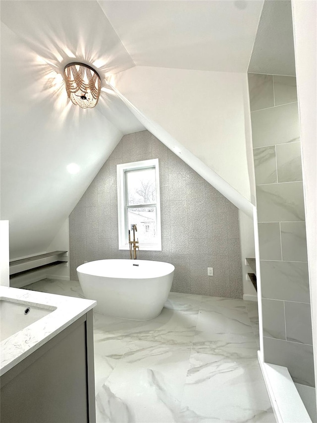 bathroom with vaulted ceiling, marble finish floor, a soaking tub, and vanity