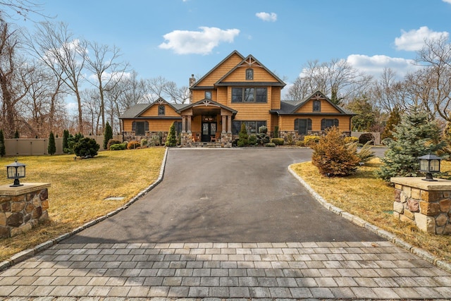 view of front facade with stone siding, driveway, a front yard, and fence