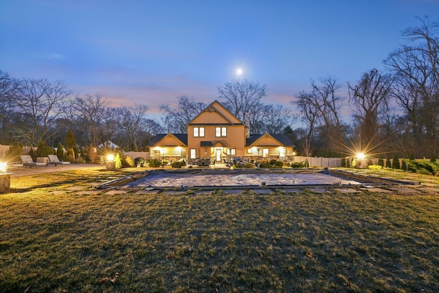 back of house at dusk featuring a yard, a patio, and fence