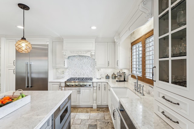 kitchen with a sink, built in appliances, stone tile flooring, and white cabinetry