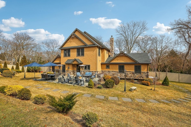 back of house with fence, a chimney, a yard, a patio area, and stone siding