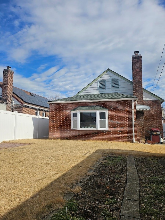 rear view of property featuring a yard, brick siding, fence, and a chimney