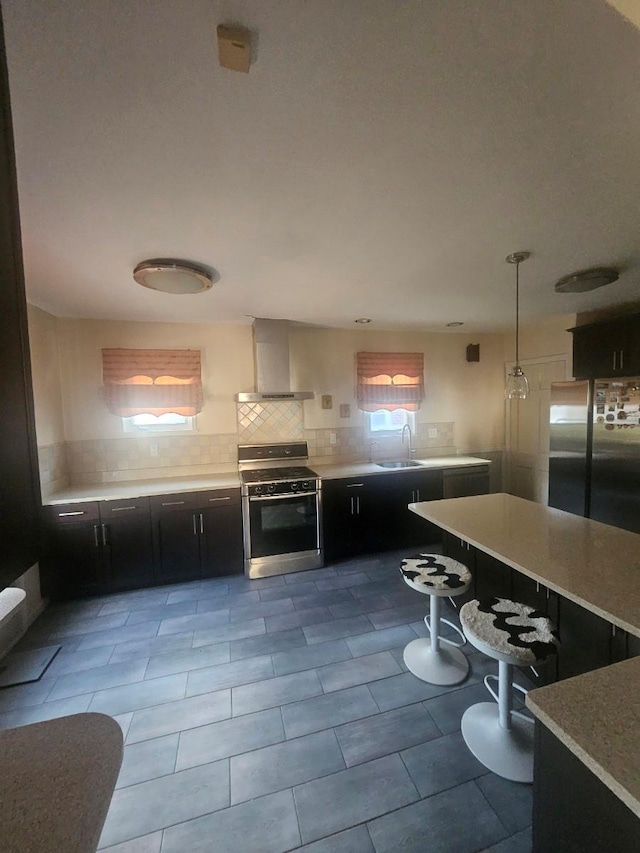 kitchen featuring a sink, wall chimney exhaust hood, appliances with stainless steel finishes, and dark cabinetry