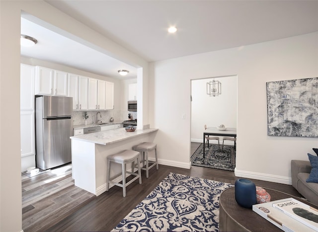 kitchen with a breakfast bar, dark wood finished floors, stainless steel appliances, decorative backsplash, and white cabinets