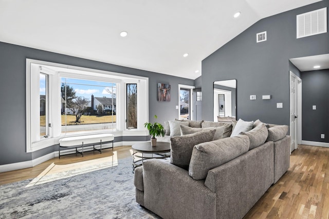 living area with visible vents, baseboards, high vaulted ceiling, and wood finished floors