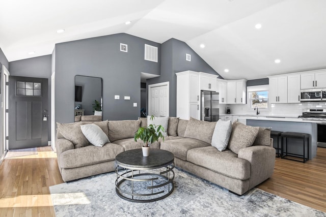 living room featuring high vaulted ceiling, recessed lighting, visible vents, and light wood-type flooring