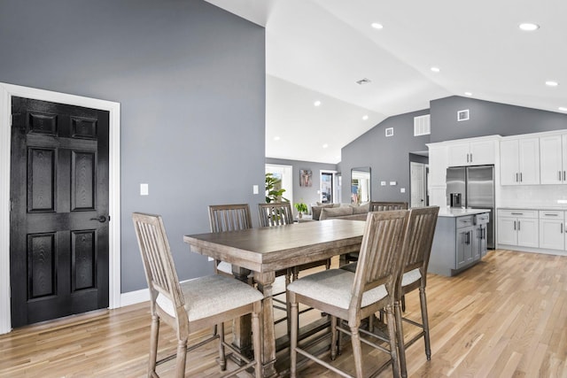 dining area featuring visible vents, light wood-style flooring, high vaulted ceiling, and baseboards