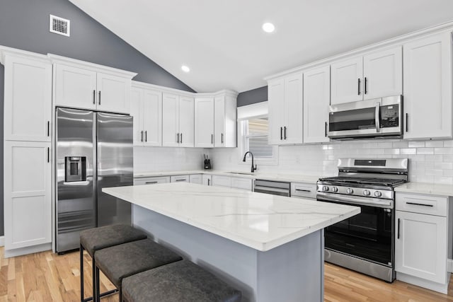 kitchen with lofted ceiling, a sink, stainless steel appliances, white cabinetry, and light wood-type flooring