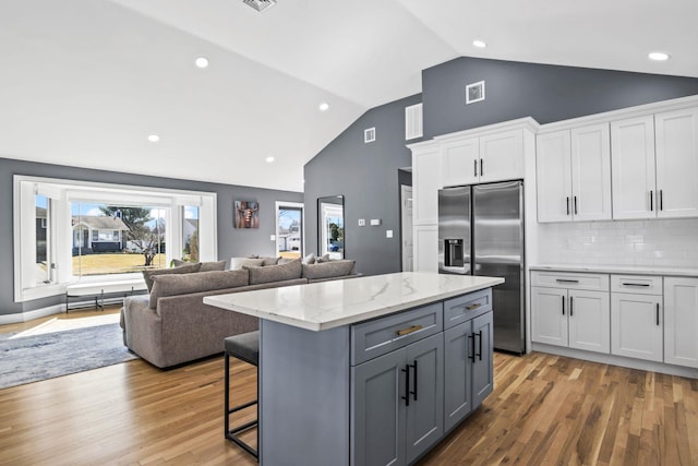 kitchen with light wood-type flooring, visible vents, stainless steel refrigerator with ice dispenser, open floor plan, and white cabinetry