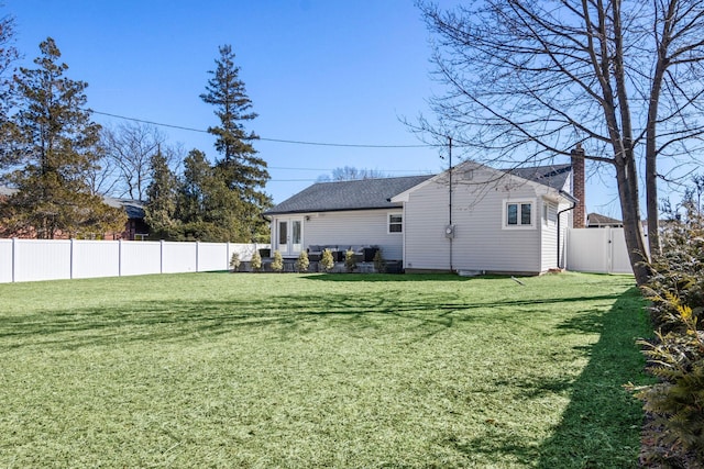 rear view of house featuring a yard, a fenced backyard, and a chimney