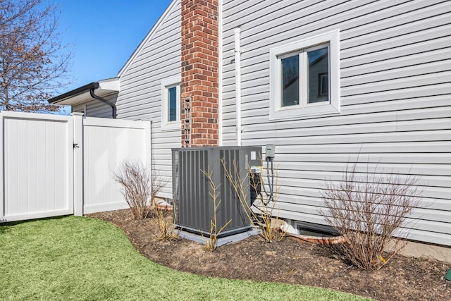 view of side of property with a gate, central AC, a chimney, and fence