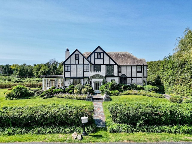 tudor-style house with a chimney and a front yard