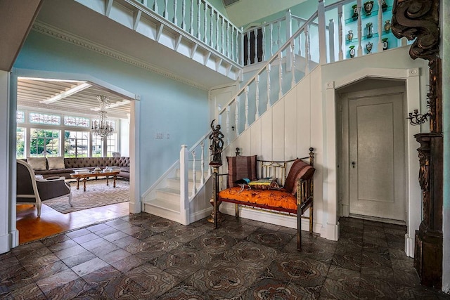 staircase featuring a towering ceiling, an inviting chandelier, stone finish floor, and baseboards