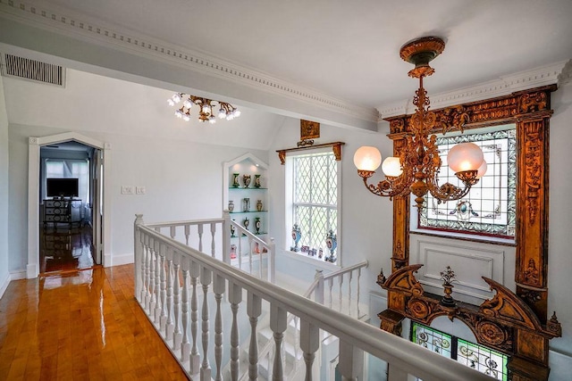 corridor with baseboards, visible vents, wood finished floors, an upstairs landing, and a chandelier