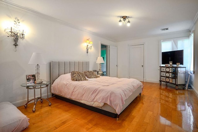 bedroom featuring ornamental molding, light wood-type flooring, visible vents, and baseboards