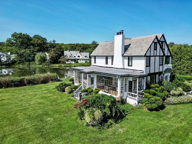 back of property with a water view, a chimney, and a lawn