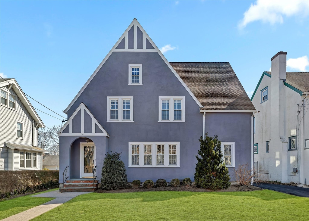 tudor house featuring stucco siding, a front yard, and roof with shingles