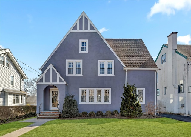 tudor house featuring stucco siding, a front yard, and roof with shingles