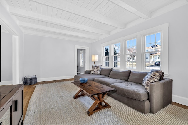 living area with baseboards, beam ceiling, wood finished floors, and wooden ceiling