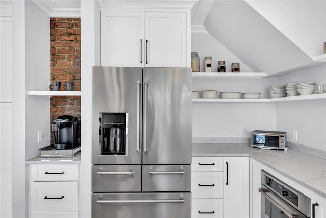 kitchen featuring light stone counters, open shelves, oven, high end refrigerator, and white cabinetry