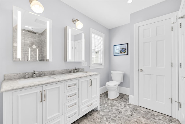 bathroom with baseboards, toilet, double vanity, tiled shower, and a sink