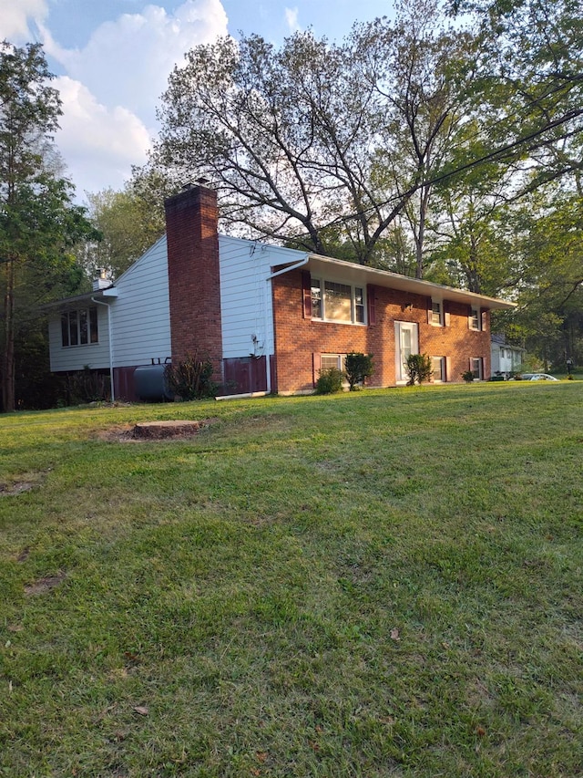 view of side of property with brick siding, a lawn, a chimney, and heating fuel