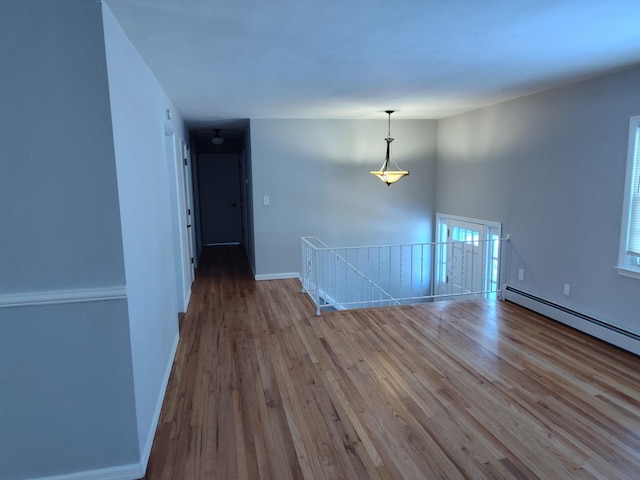 empty room featuring a baseboard radiator, baseboards, and wood finished floors