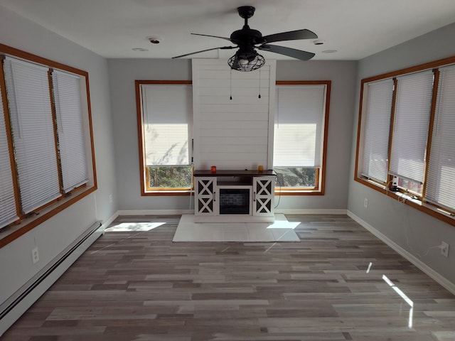 unfurnished living room with a baseboard radiator, baseboards, a wealth of natural light, and wood finished floors