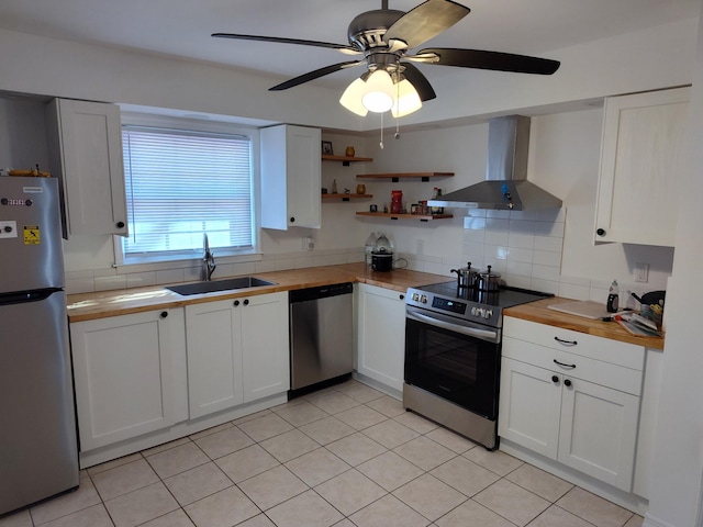 kitchen featuring wall chimney exhaust hood, wood counters, appliances with stainless steel finishes, white cabinetry, and a sink