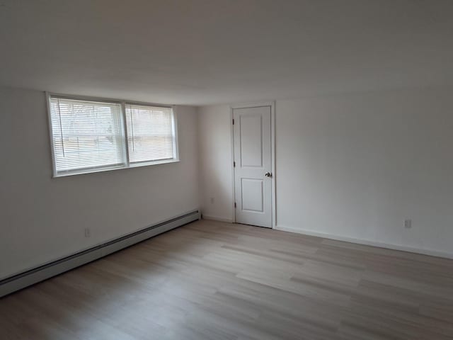 spare room featuring a baseboard radiator, baseboards, and wood finished floors