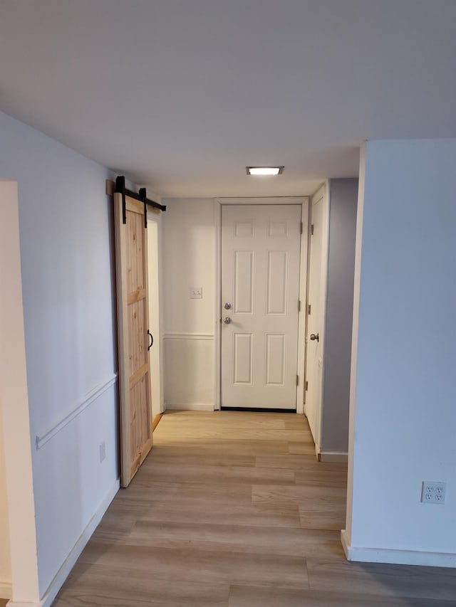 corridor with light wood finished floors, a barn door, and baseboards