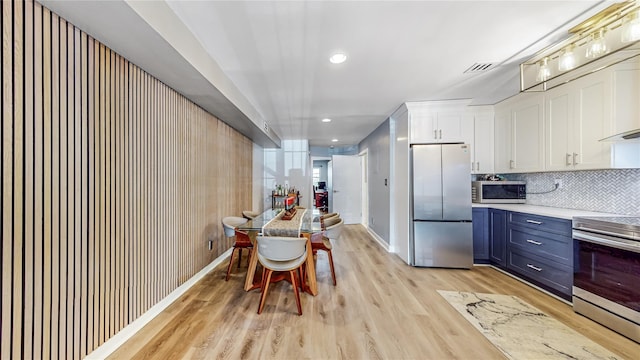 kitchen with stainless steel appliances, light countertops, decorative backsplash, light wood-style floors, and white cabinets