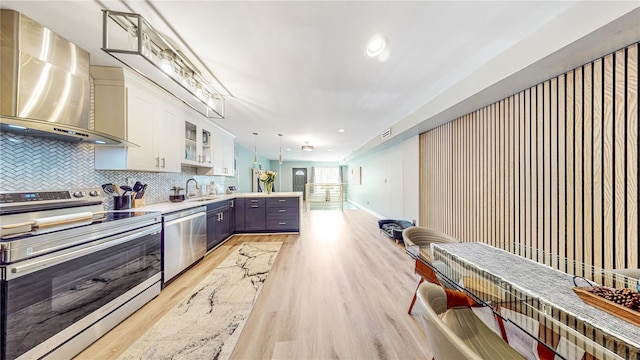 kitchen with decorative backsplash, a peninsula, stainless steel appliances, wall chimney range hood, and white cabinetry