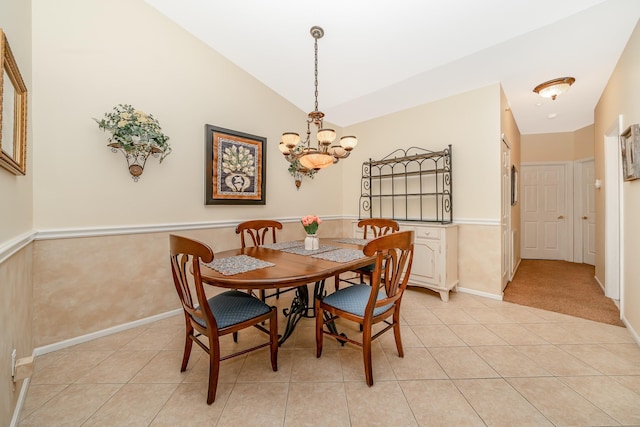 dining space with light tile patterned floors, a chandelier, wainscoting, and lofted ceiling