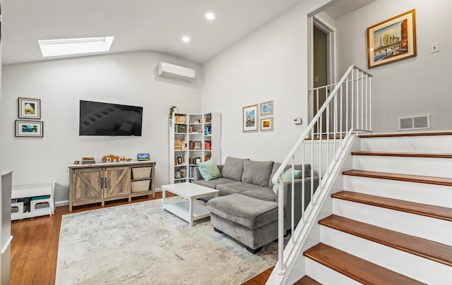 living area featuring visible vents, stairway, an AC wall unit, vaulted ceiling with skylight, and wood finished floors