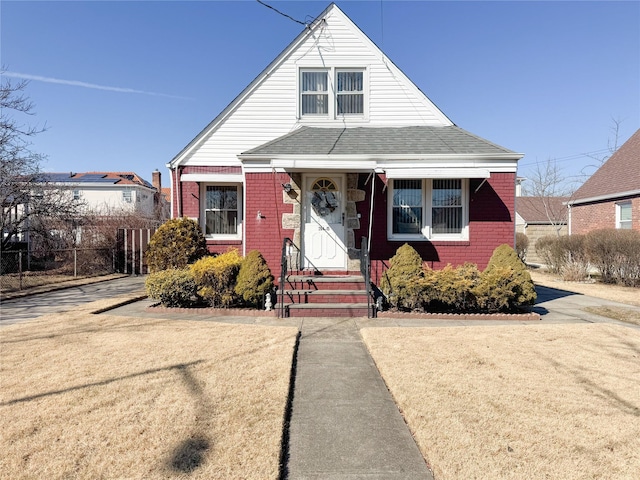 bungalow featuring a shingled roof, a front yard, fence, and brick siding