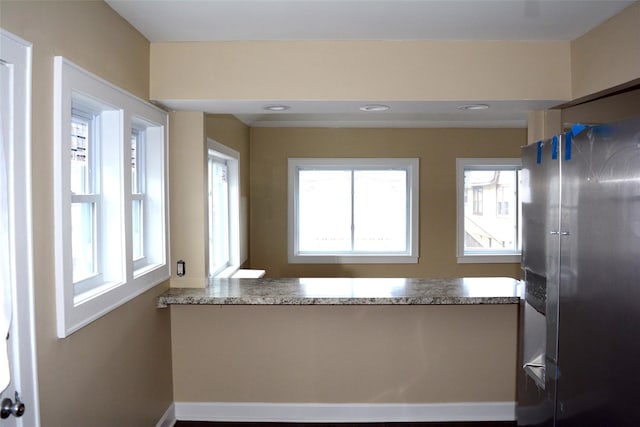 kitchen with a peninsula, light stone counters, and stainless steel fridge with ice dispenser