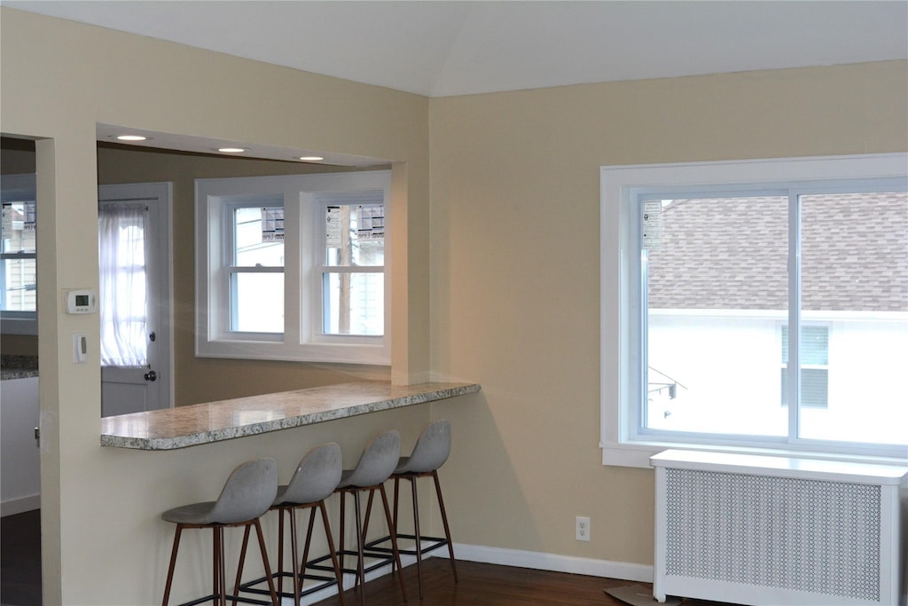 kitchen with dark wood-style floors, a breakfast bar area, radiator, light countertops, and baseboards