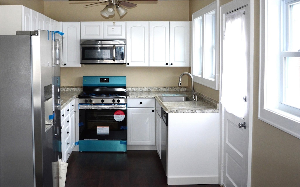 kitchen with appliances with stainless steel finishes, a sink, white cabinetry, and a healthy amount of sunlight