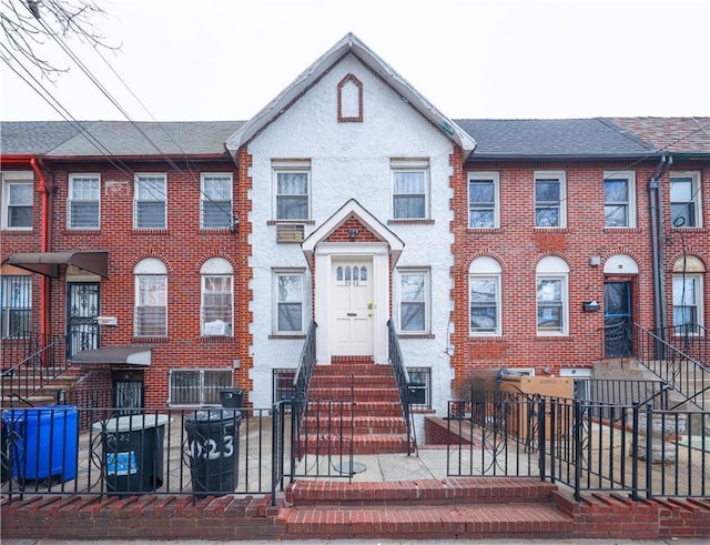 townhome / multi-family property featuring stucco siding, a fenced front yard, a shingled roof, and brick siding