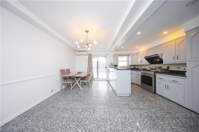 kitchen featuring a wall mounted air conditioner, a notable chandelier, stainless steel gas range, a tray ceiling, and dark countertops