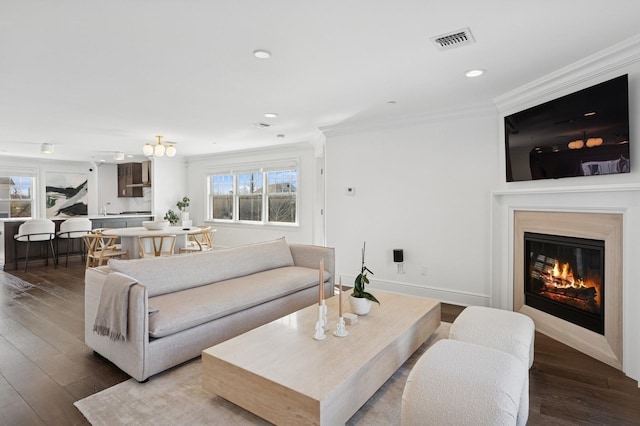 living room featuring a glass covered fireplace, wood finished floors, visible vents, and crown molding