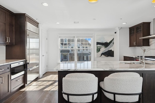 kitchen with visible vents, light wood-style flooring, dark brown cabinetry, light stone countertops, and built in appliances