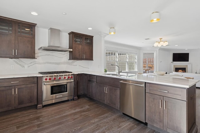 kitchen with a peninsula, stainless steel appliances, dark wood-style flooring, a sink, and wall chimney exhaust hood