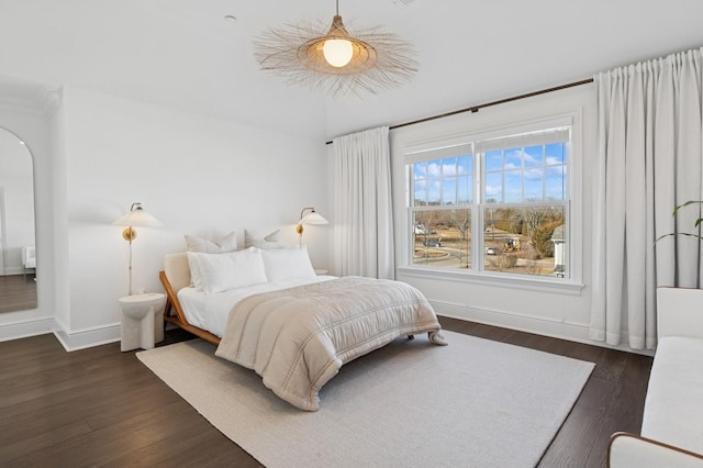 bedroom featuring arched walkways, dark wood finished floors, and baseboards