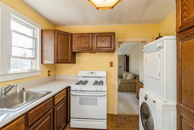 kitchen with stacked washer / dryer, white gas range, a sink, and brown cabinetry