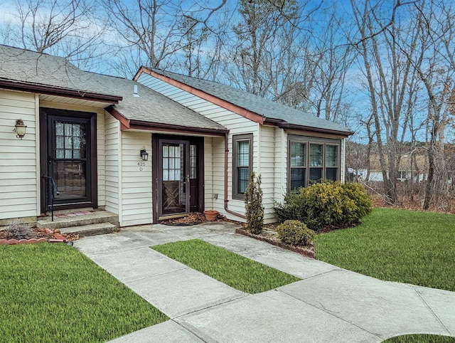 doorway to property featuring a shingled roof and a lawn