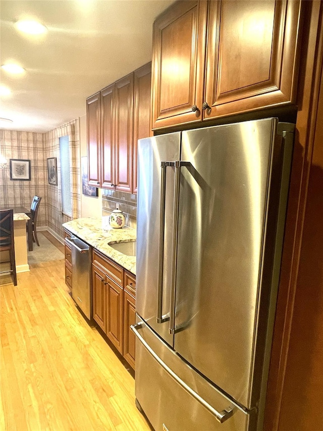 kitchen with light wood finished floors, wallpapered walls, baseboards, light stone counters, and stainless steel appliances