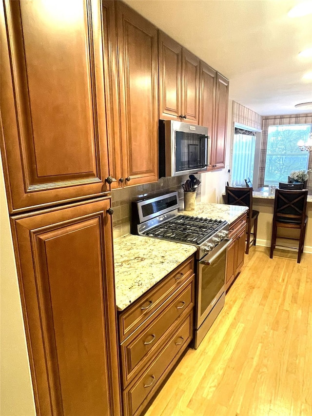 kitchen with light stone counters, stainless steel appliances, light wood-style flooring, brown cabinetry, and baseboards